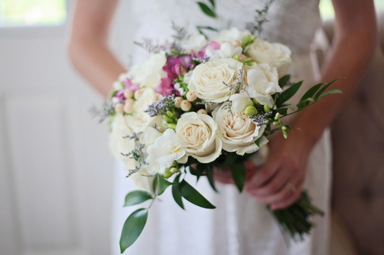 A bride holding a tasteful bouquet of white roses with a few fuschia colored flowers throughout