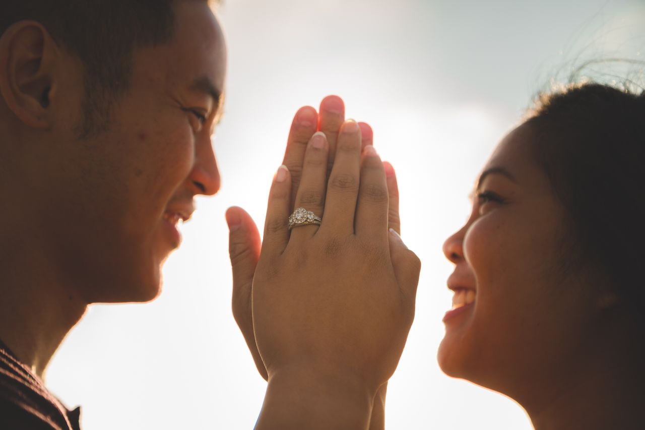 Married couple holding hands, with three stone halo engagement ring visible