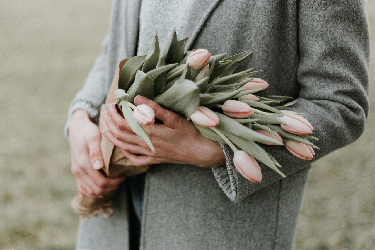 Woman in a gray coat holding a bouquet of pink tulips