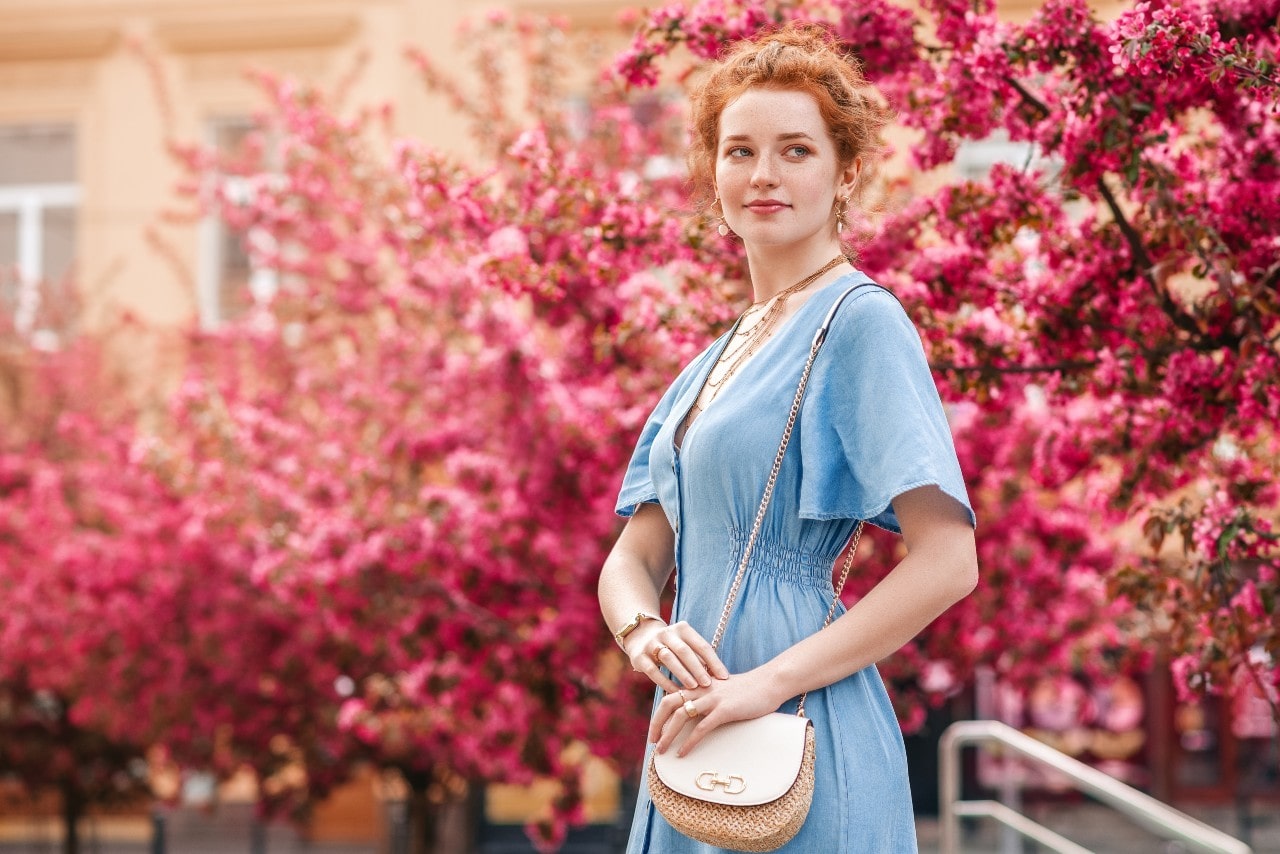 Fashionable lady wearing fancy earrings, a bracelet, and a necklace standing in front of colorful pink bushes