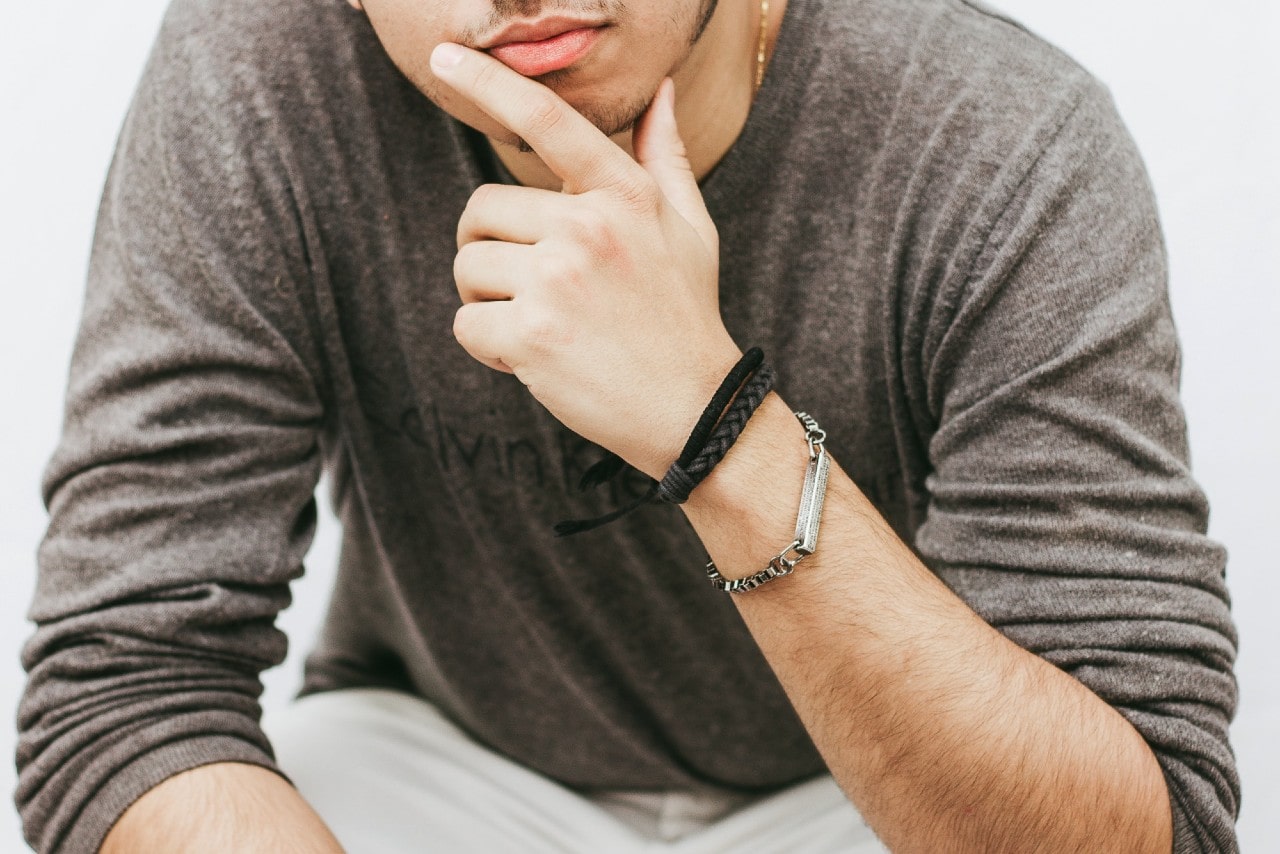 A pondering man leans forward and shows off his black braided and sterling silver bracelets