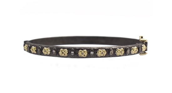 A bangle bracelet wrought in a dark metal and featuring yellow gold details