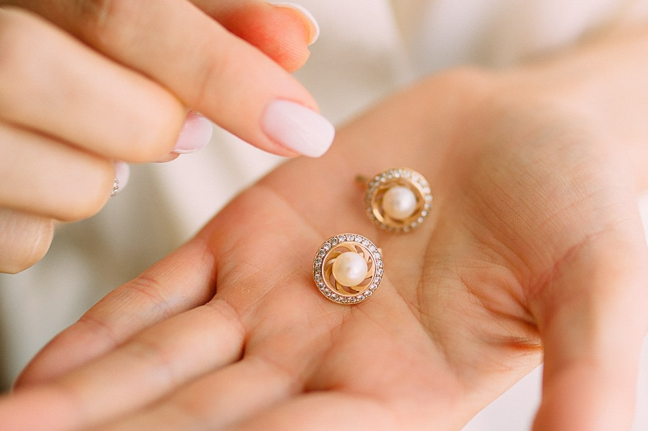 A close-up of a woman’s hands, with stunning pearl stud earrings in her open palm.