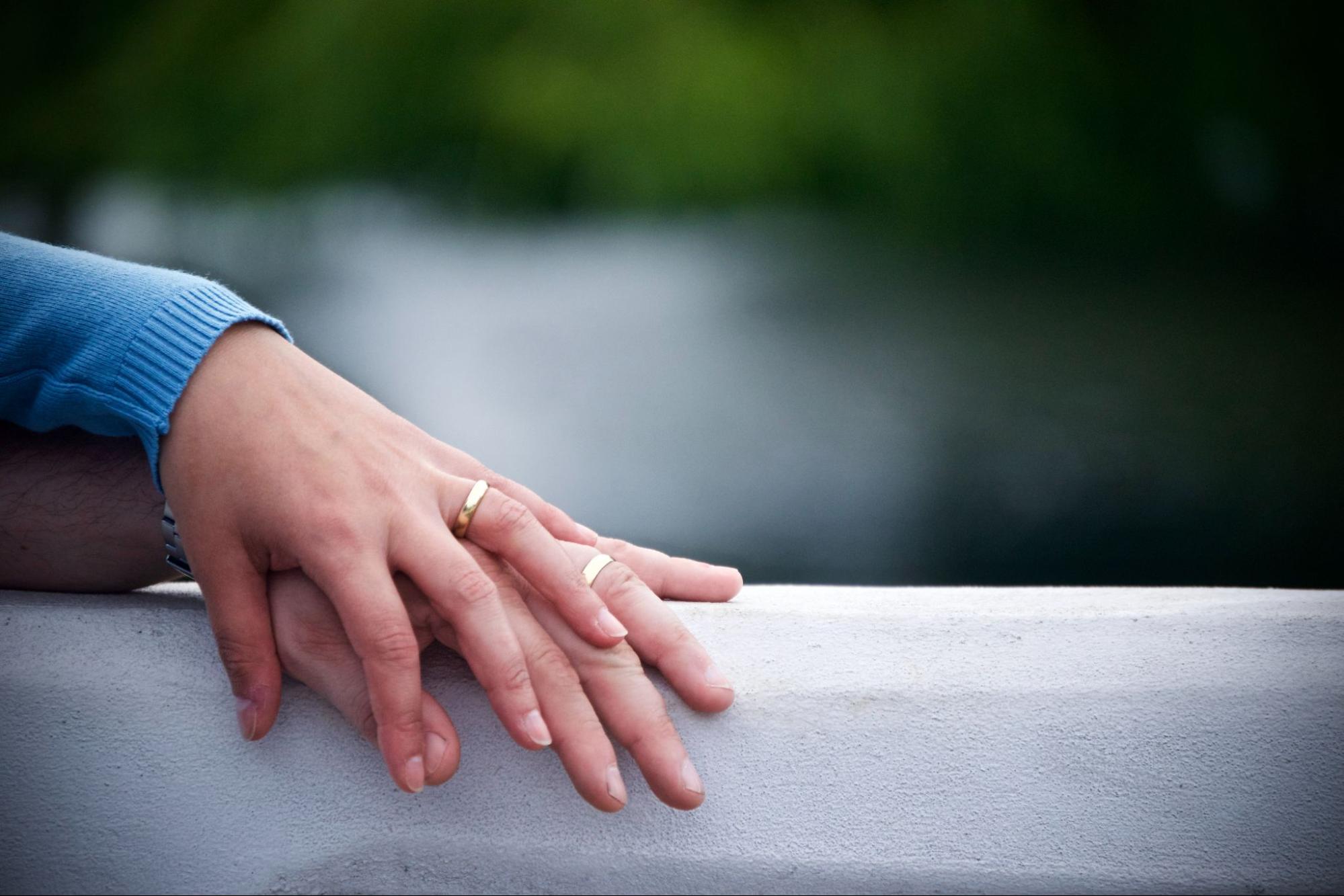 A married couple’s hands lay on top of each other with matching bands.