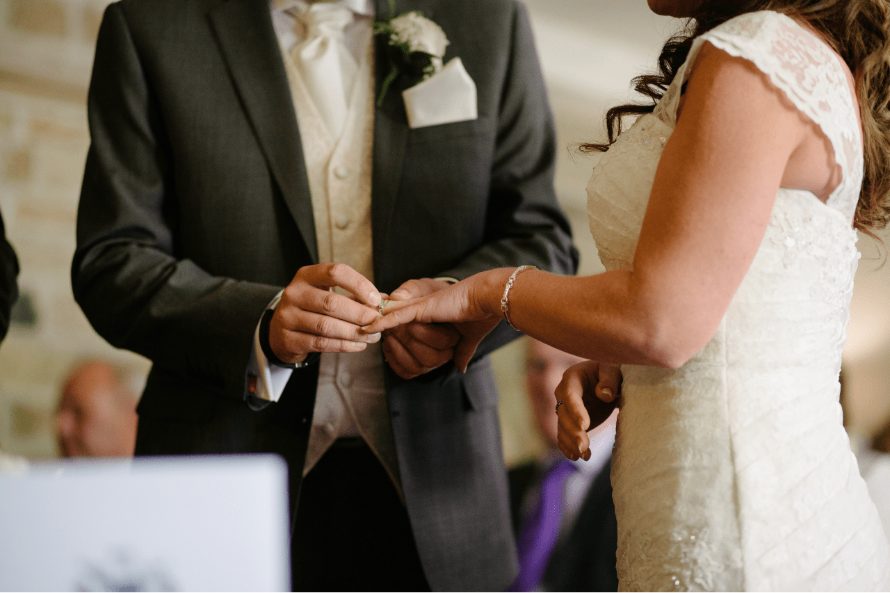 A groom slips a ring on his bride’s finger during a ceremony.