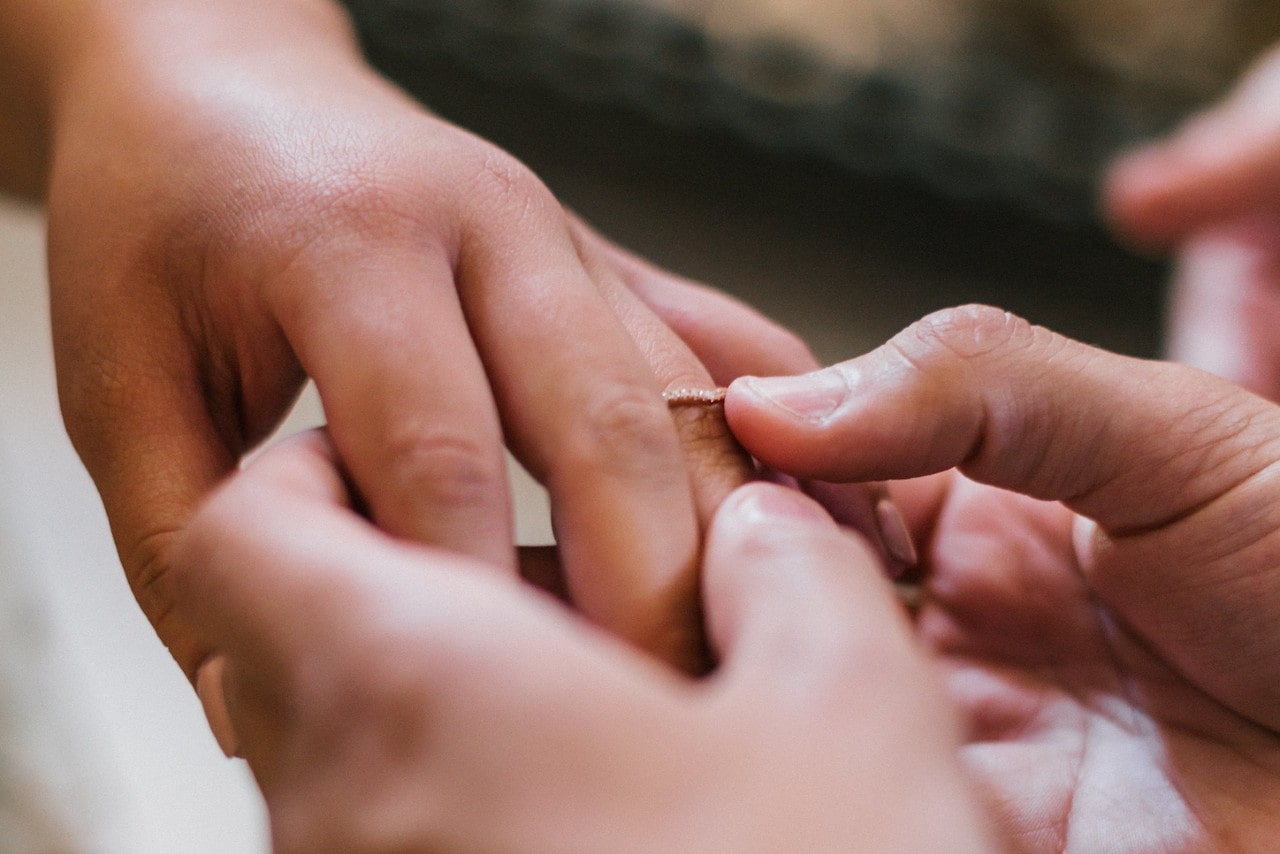 A groom slips a wedding band on his bride’s ring finger.