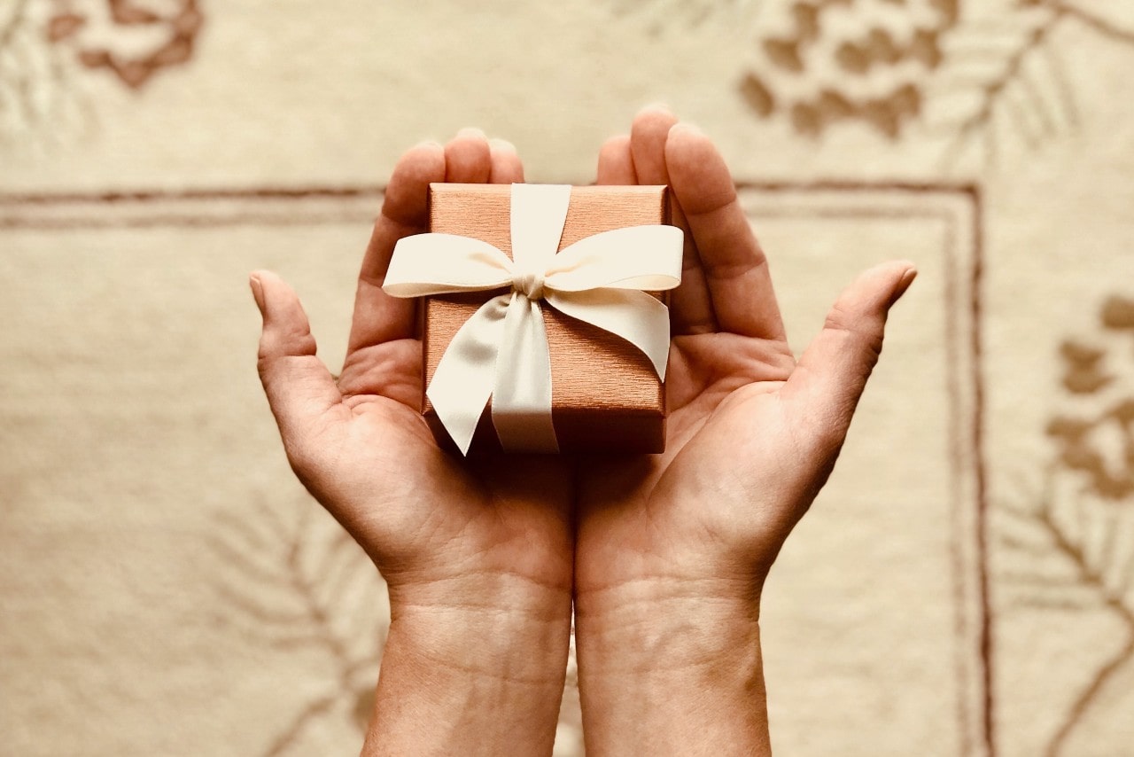 A close-up of a small, elegantly wrapped gift held in a person’s hands.