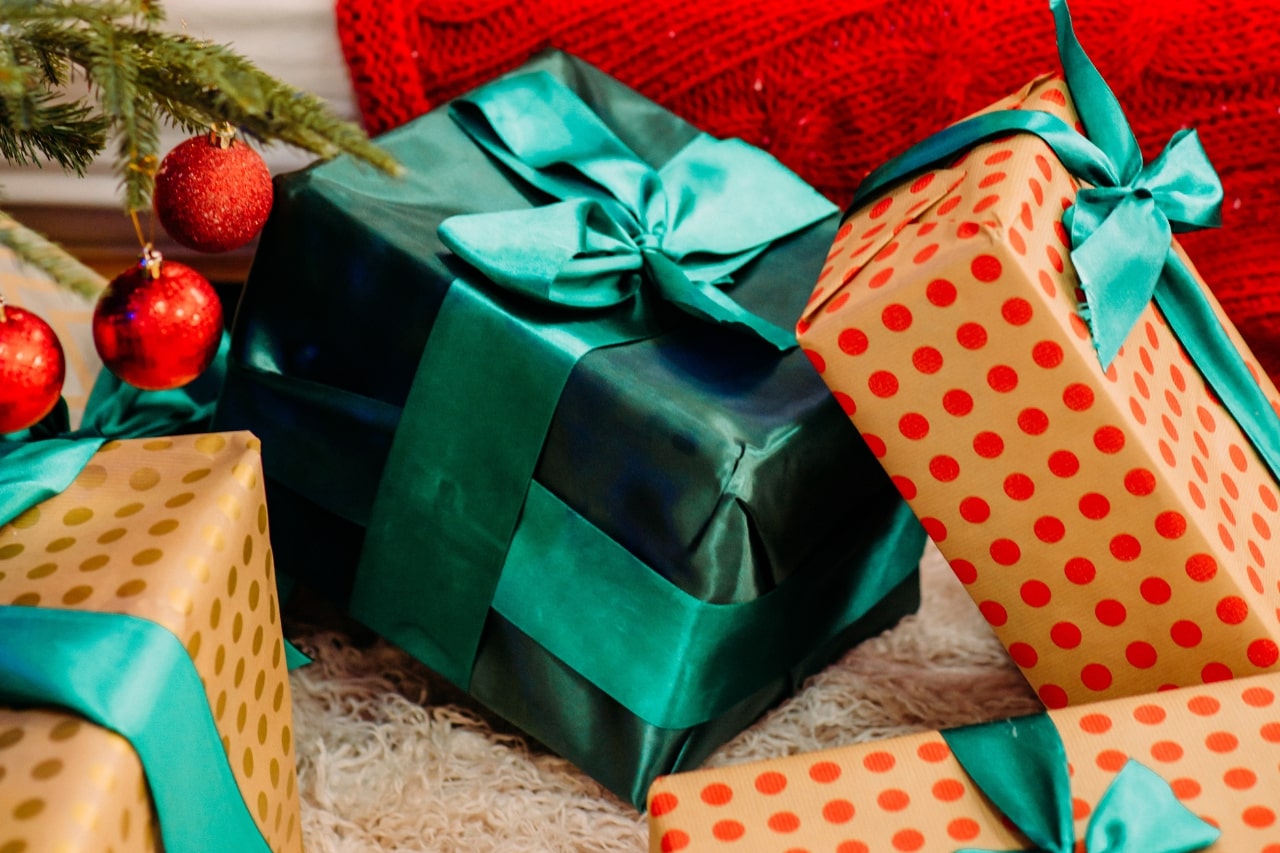 A close-up of multiple colorful presents, each wrapped with green ribbon, under a Christmas tree.