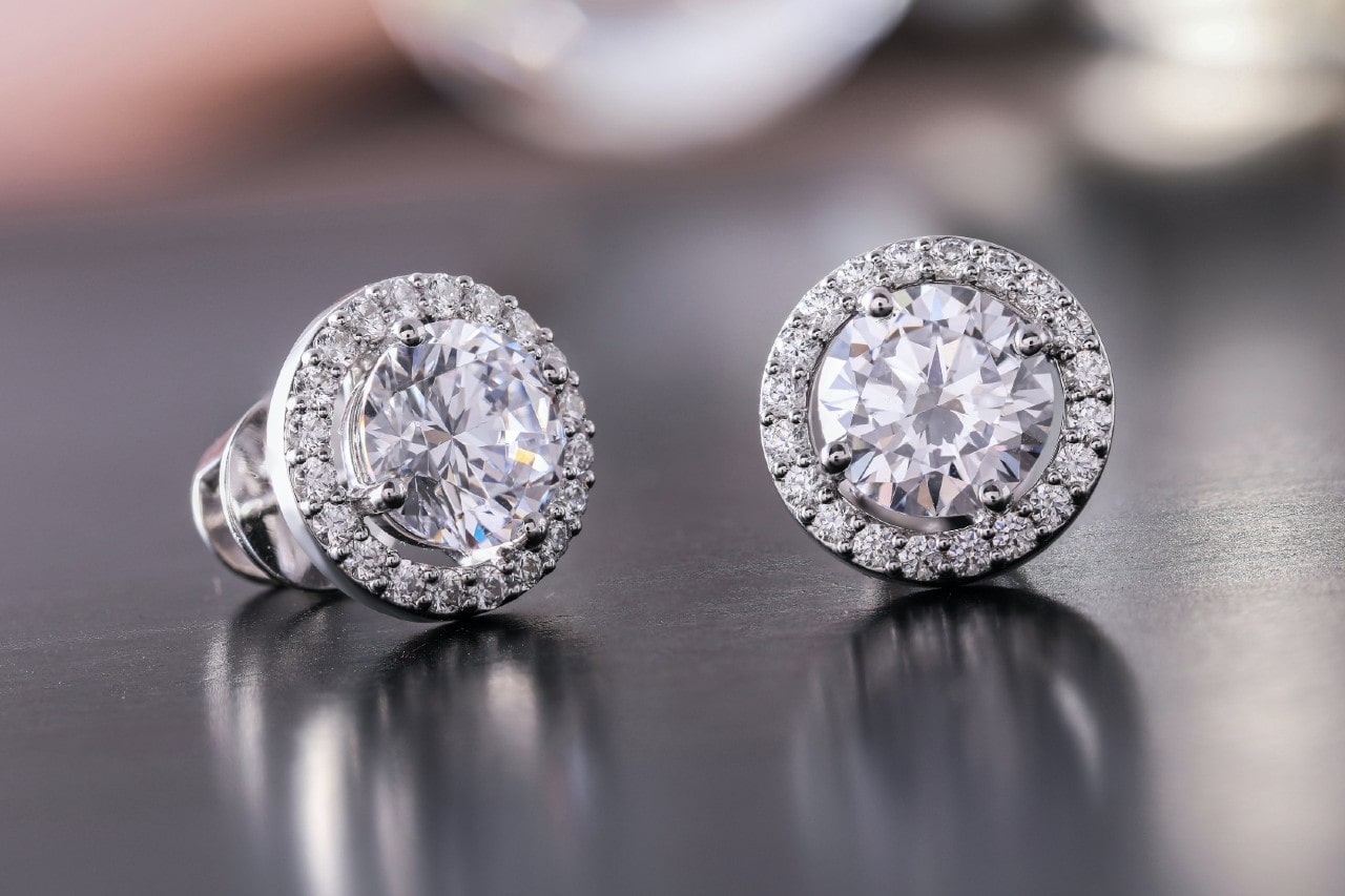 a pair of round cut diamond halo stud earrings on a metallic surface