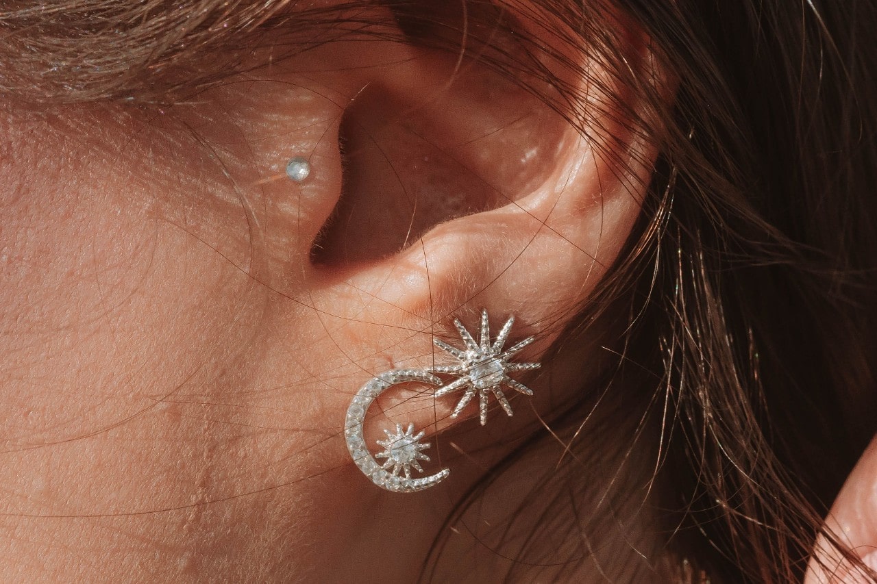 close up image of a woman’s ear studded with two diamond stud earrings in a star and moon shape