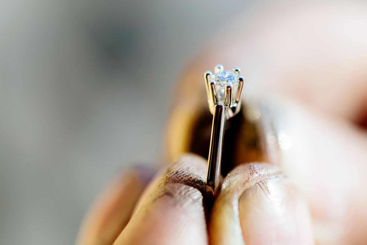 A close-up of a diamond ring held delicately between fingers, highlighting the intricate details of the setting