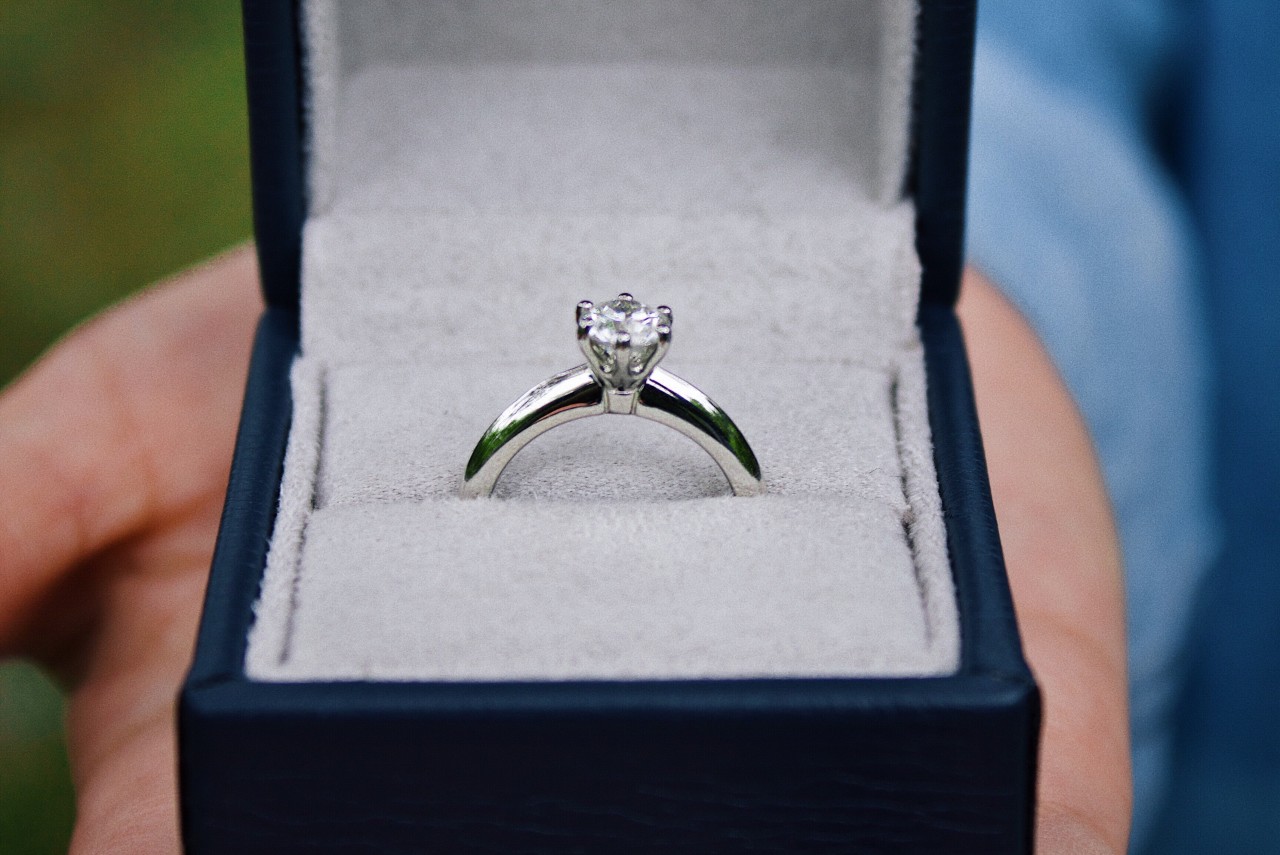 A solitaire diamond ring is presented in an open navy-blue ring box with a soft gray interior