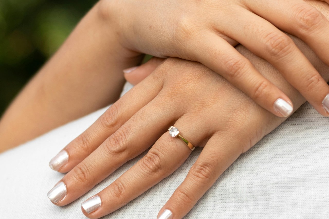 A close-up of a bride-to-be’s hands, adorned with a simple solitaire engagement ring.