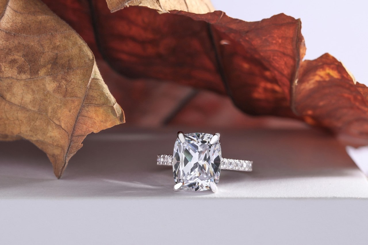 A stunning engagement ring displayed in front of crisp fall leaves on a white pedestal.