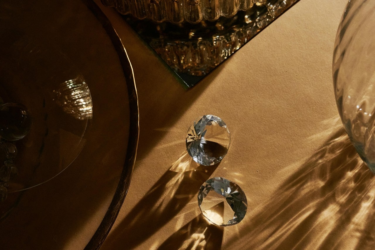 two round cut diamonds sitting on a beige table next to pieces of glassware