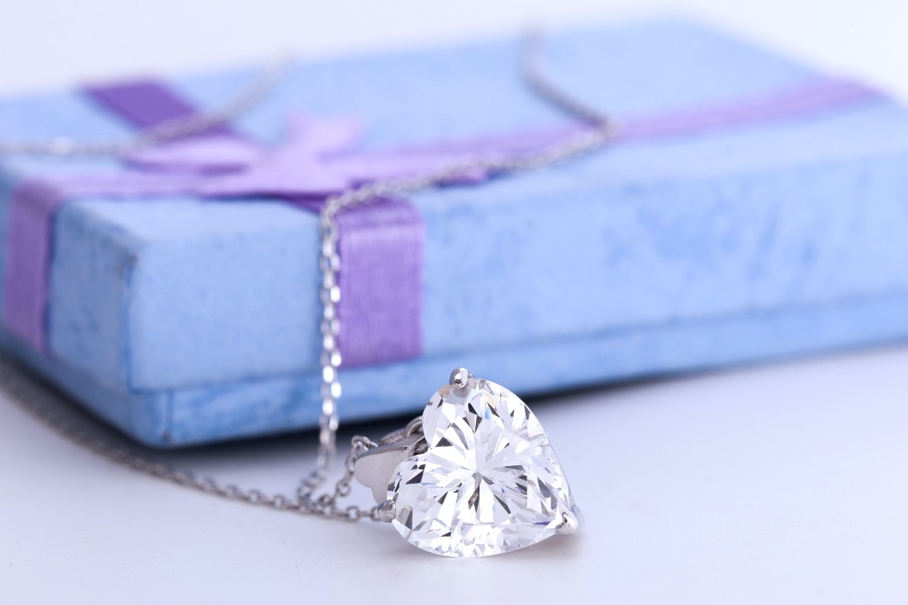 A heart-shaped necklace from Clarkes Jewelers draped over a gift box.