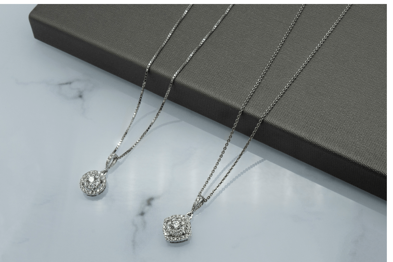 Two diamond solitaire pendants displayed off the side of a gray box.