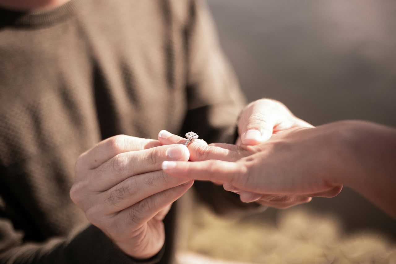 A man placing a diamond engagement ring on a woman’s ring finger.