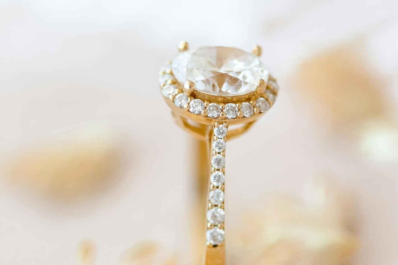 a yellow gold, oval cut halo engagement ring with prong set side stones.