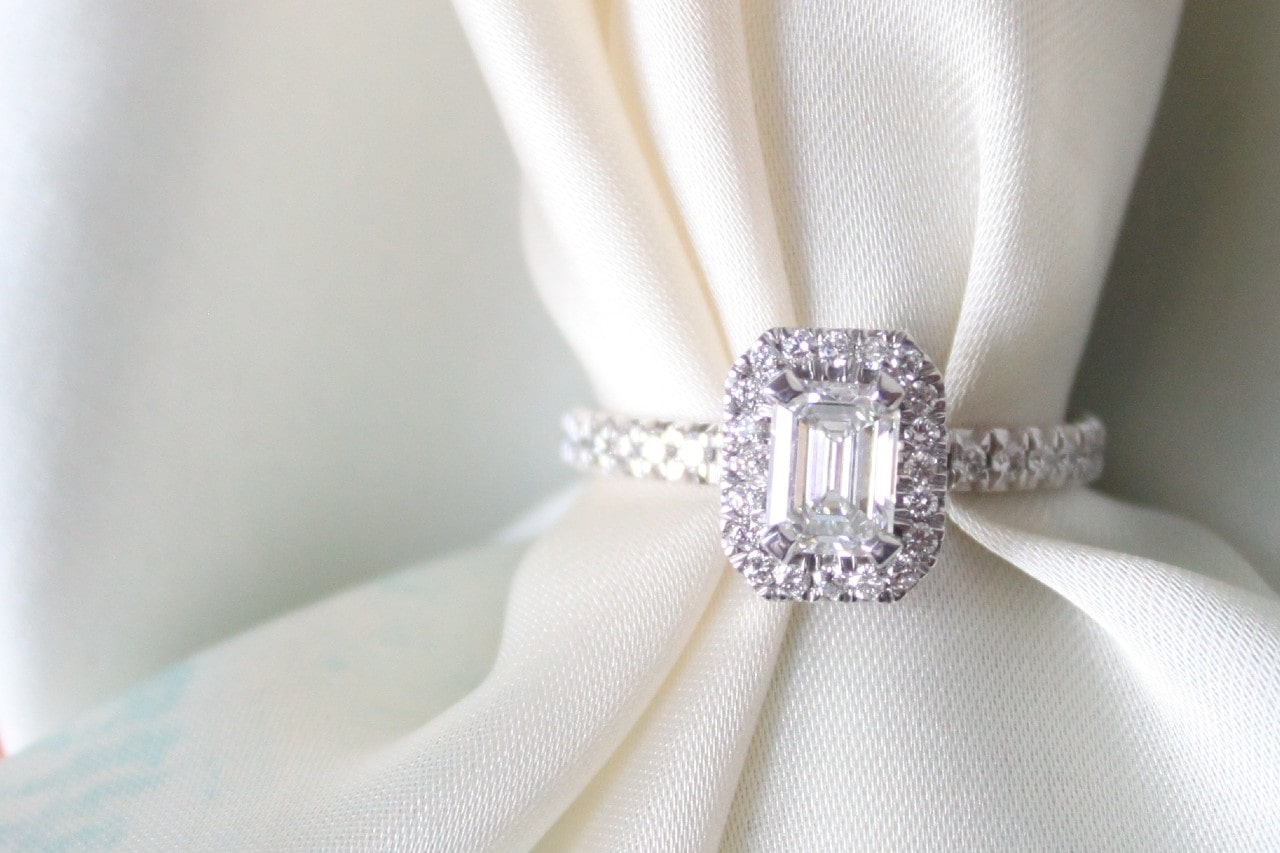 a white gold emerald cut halo engagement ring with side stones with white fabric threaded. through