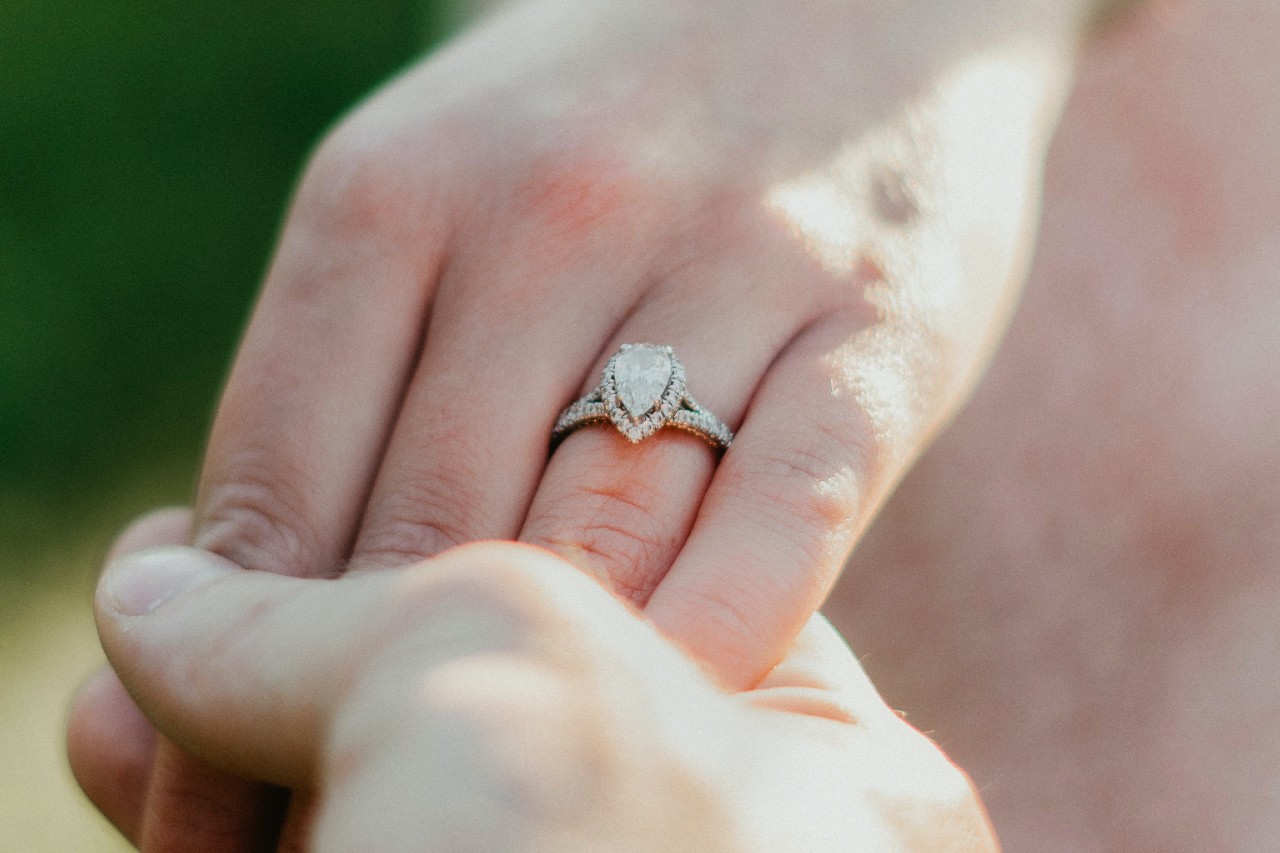 a woman’s hand being held by a man’s and adorned with a pear shape engagement ring.