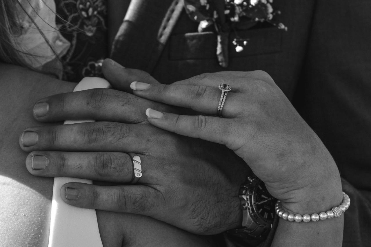 and bride and groom’s hands resting on her shoulder, the bride wearing a matching bridal ring set